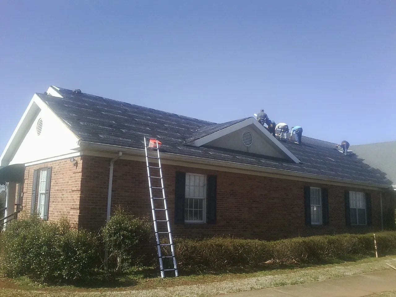 Crew tearing shingles off a brick ranch roof with a ladder set — Metal Roof Repair work by our crew in Somis