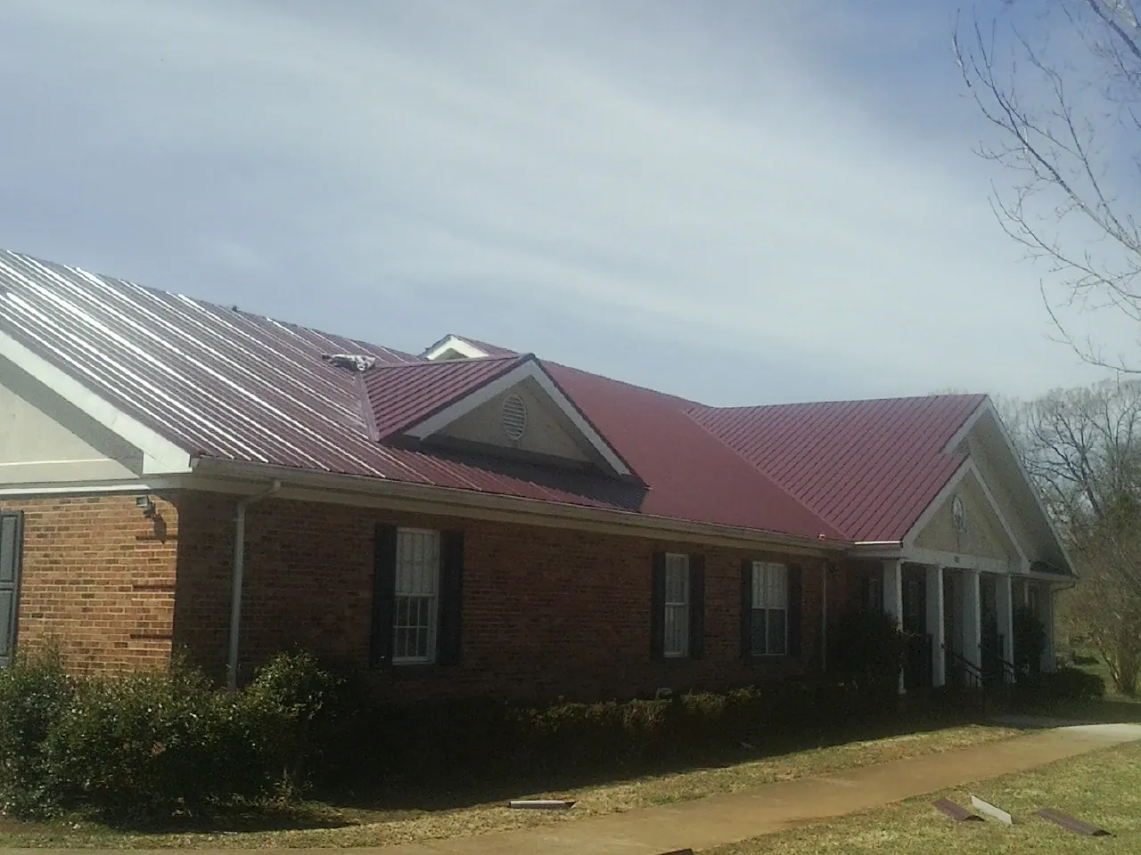 Red metal roof with gabled entries on a long brick building, from a Hail Damage Roof Repair job in Somis