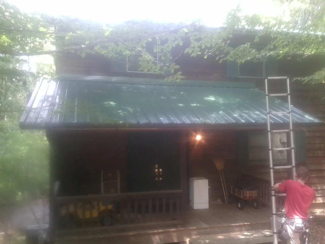 Worker on a ladder at the green porch roof of a wooded cabin in Somis