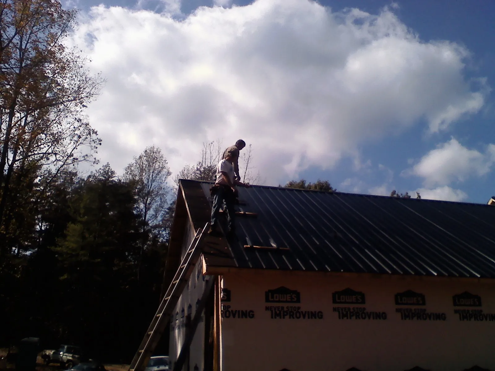 Roofer fastening dark metal panels high against a cloudy sky, from a Roof Inspection job in Somis